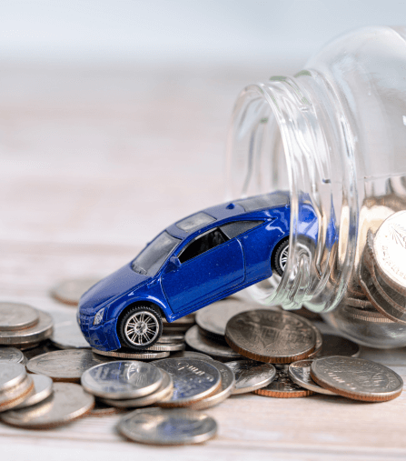 Small blue toy car on top of stacked coins spilling from a glass jar