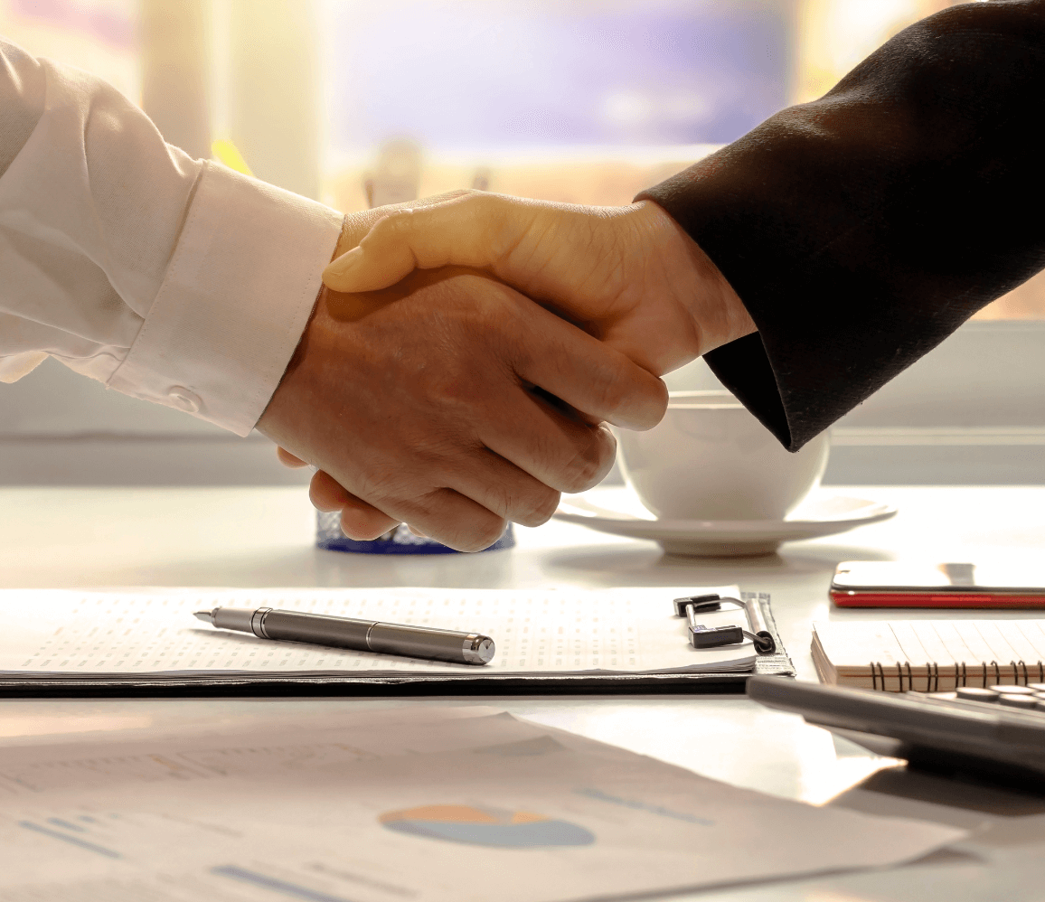 Close-up of two professionals shaking hands over financial documents